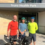 Three people standing with bicycles outside Truro Health Park.